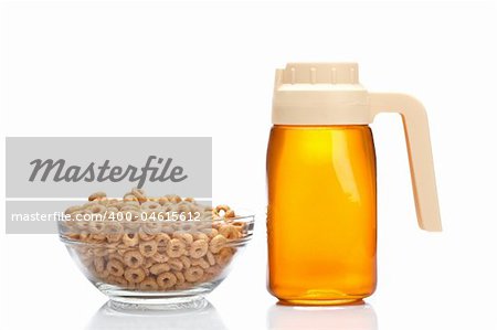 Honey pitcher and glass bowl of cornflakes, reflected on white background