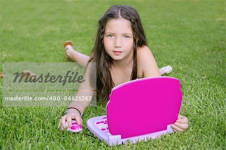 Beautiful little girl playing with pink toy computer outdoor in grass