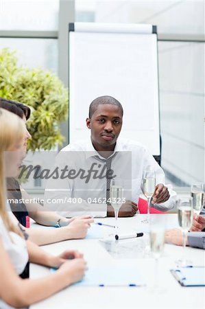 Afro-American businessman drinking champagne in office with his team