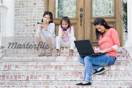 Mère en utilisant l'ordinateur portable et des filles à l'aide de jeux vidéo portables