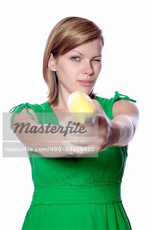 Pretty girl in a green dress is holding a banana as a gun, isolated on white