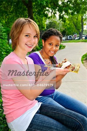 Two teenage girls sitting and eating pizza