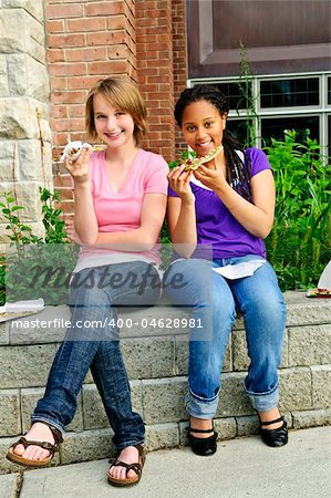 Two teenage girls sitting and eating pizza