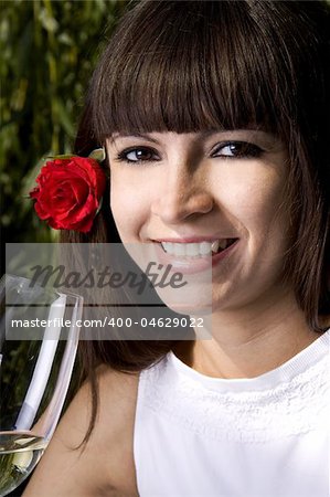 Beautiful brunette with a rose in her ear is enjoying white wine