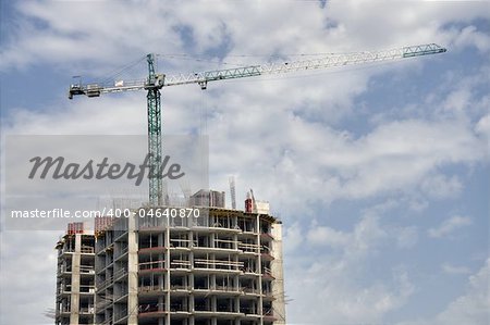 steel crane above incomplete building, sky with clouds