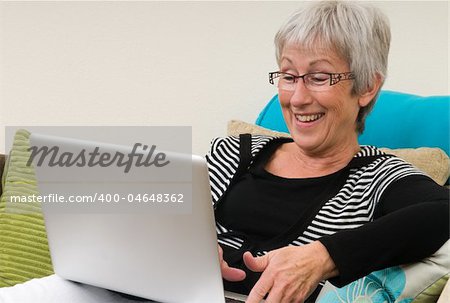 Senior woman working on a laptop, sitting relaxed on the couch.
