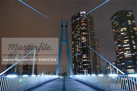 well illuminated suspension bridge  by night with pedestrians shadows between residential skyscrapers in Tokyo