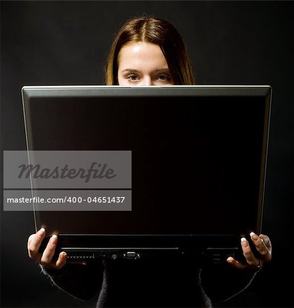 young beautiful girl as anonymous computer user with notebook on black background and hidden face