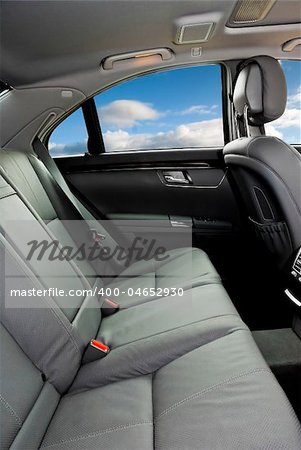 Backseat grey leather interior of a luxury car with blue skies through the windows