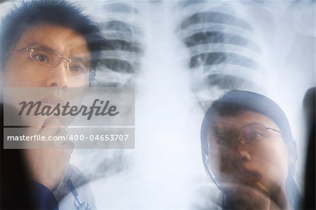 Asian doctor examining xray negative / roentgen print. PS:the image taken from behind the xray print, so it may leave some soft noise on the people image behind it.