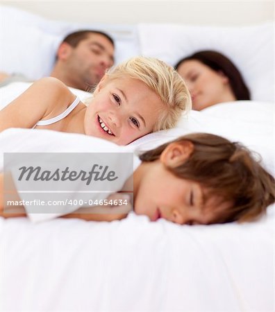Beautiful little girl smiling on bed wile her family sleep