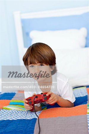 Young boy playing videogames sitting in his bed