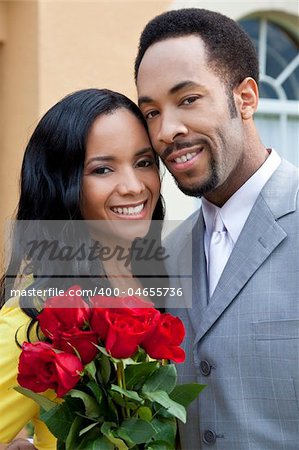 A romantic and happy African American man and woman couple in their thirties smiling together with a bunch of roses.