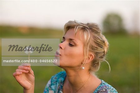 Beautiful blond girl blows dandelion seeds for luck
