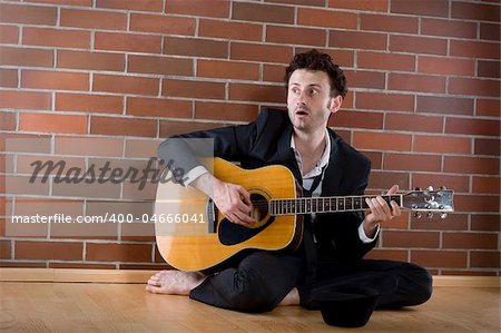 desperate businessman sits with a guitar on the floor and sings fort money