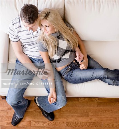 Cropped overhead view of affectionate couple sitting together on white love seat. Square format.