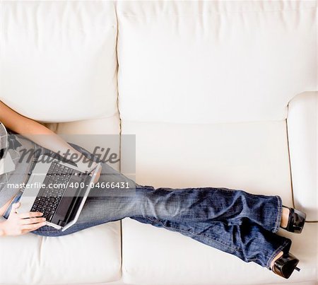 Cropped overhead view of woman reclining on white couch and using a laptop. Horizontal format.