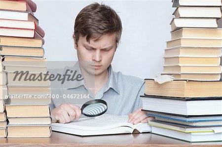 Young surprised student reading book with loupe between books