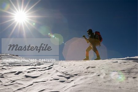 Man of mountain climber walk in snow winter day with sun light flare.
