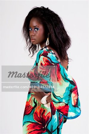 Attractive young woman wearing a colorful print dress. She is standing with one hand on her hip and looking back towards the camera. Vertical shot.