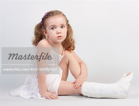 Little girl injured with broken ankle sitting on white backgound.