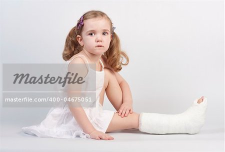 Little girl injured with broken ankle sitting on white backgound.