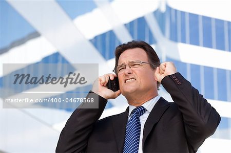 Excited Businessman Using Cell Phone Clinches His Fist in Joy Outside of Corporate Building.