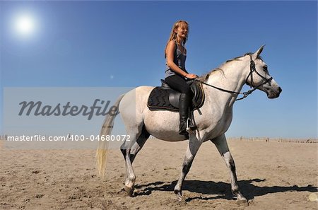 young teen and her white horse on the beach, sun with halo in the sky