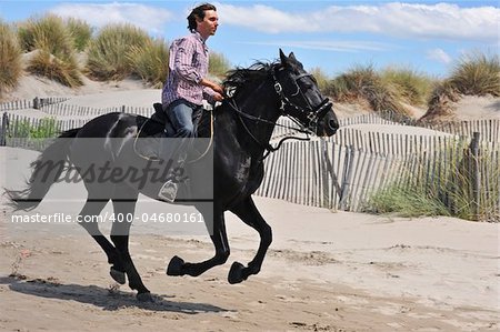 galloping black stallion and his rider on the beach