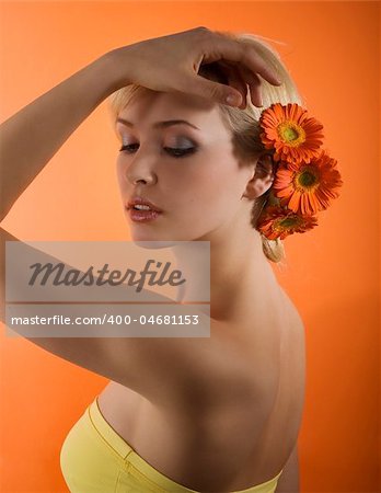 cute blond girl posing against orange beckground with some gerbera flowers on her head