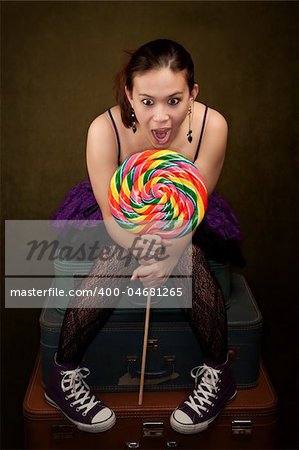 Pretty girl in funky purple outfit on green background with big lollipop