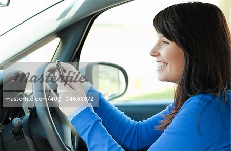 Smiling brunette teen girl using a mobile phone while driving