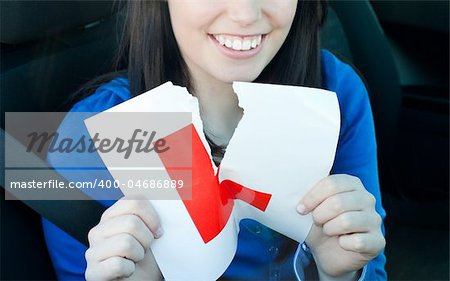 Charming teen girl sitting in her car tearing a L-sign after having her driver's licence