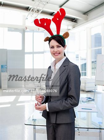 Smiling businesswoman with a novelty Christmas hat drinking Champagne in the office