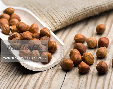 Hazelnuts Spilling Out Of A Wooden Scoop Onto A Table With A Hessian Bag In The Background