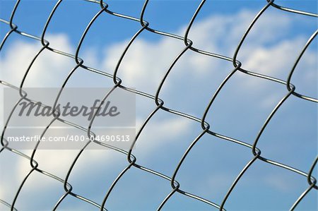 Metal wire fence against blue sky with clouds