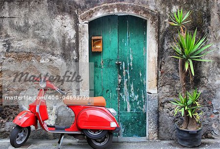 Photo of red scooter near green door and palm
