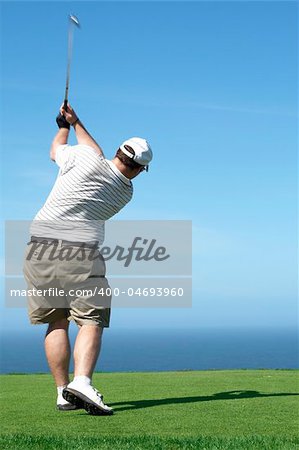 Young male golfer hitting the ball from the tee box next to the ocean on a beautiful summer day