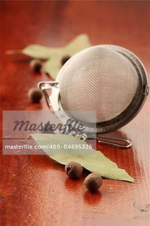 Allspice, bay leaf and tea strainer on a wooden background