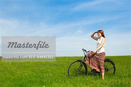 Happy young woman with a vintage bicycle on a green meadow