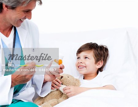 Smiling little boy taking cough medicine lying in a bed