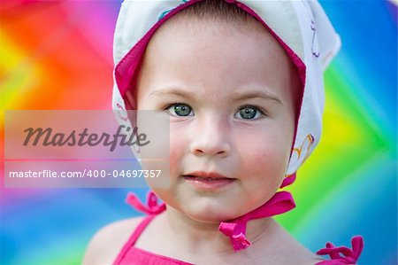 Small baby girl hiding under a big colorful umbrella at a picnic