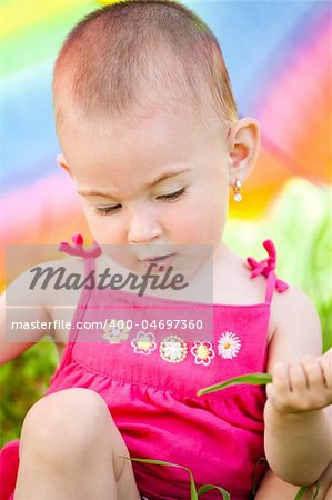 Small baby girl hiding under a big colorful umbrella at a picnic