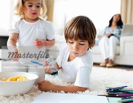 Adorable children eating chips and drawing lying on the floor