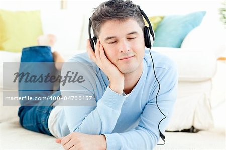 Handsome young man listening music lying on the floor at home