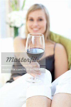 Radiant woman drinking red wine siting on a sofa