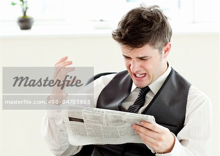 Portrait of a annoyed businessman reading a newspaper in the office against white background