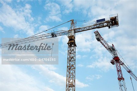 Cranes of a construction site against blue, cloudy sky