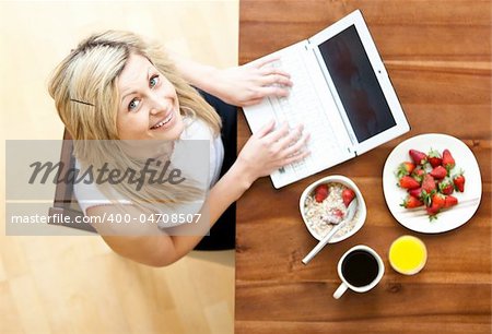 Close-up of a woman using a laptop drinking coffee eating muesli