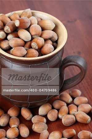 Ceramic mug with spilled different-sized hazelnuts on a wooden table